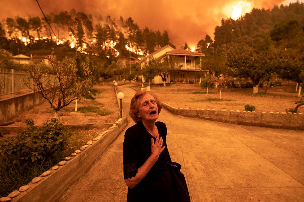 An elderly woman cries out as a wildfire approaches her house in the village of Gouves, on the island of Evia, Greece, on 8 August 2021