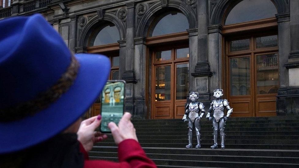 A woman takes a photo of cybermen outside the National Museum of Scotland