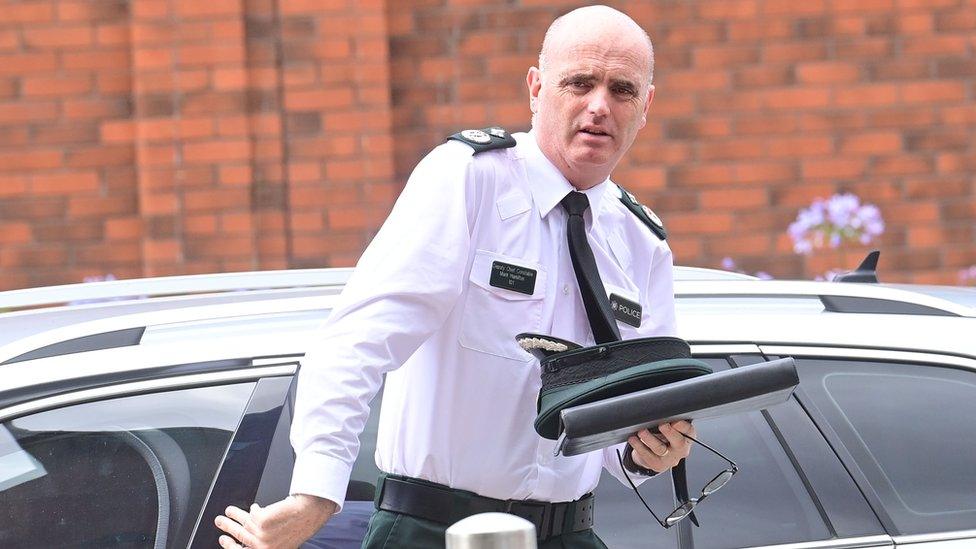 Deputy Chief Constable Mark Hamilton gets out of a car holding his police uniform cap in his left hand on top of a document file