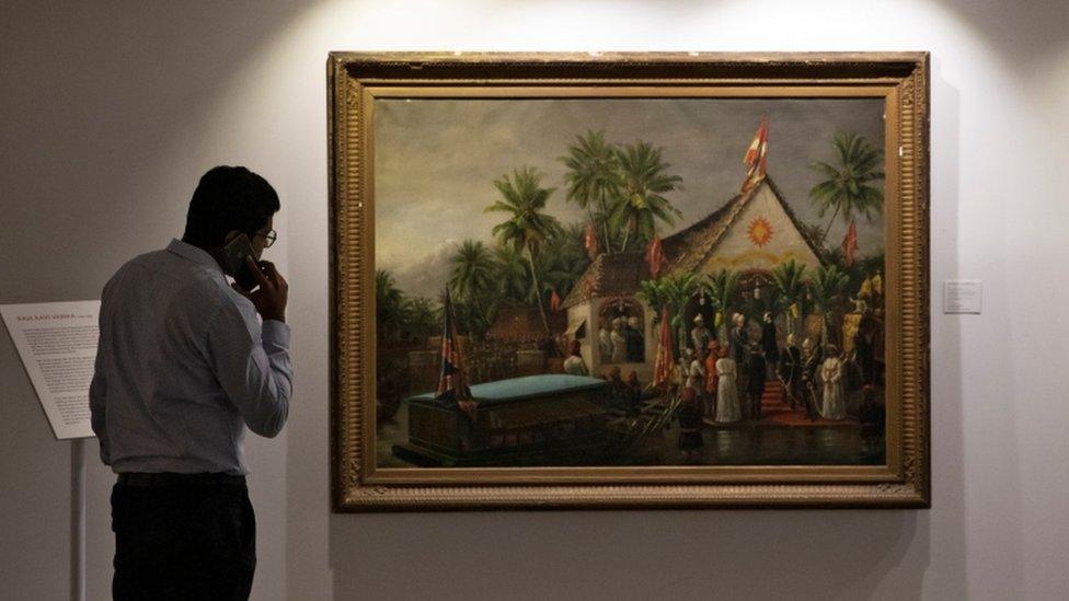 A man on the phone looks at Raja Ravi Varma's paining