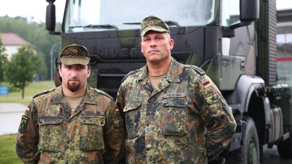 Corporal Christopher Seidel (L) and Staff sergeant Friedemann Frischko (R) stand in front of their army truck