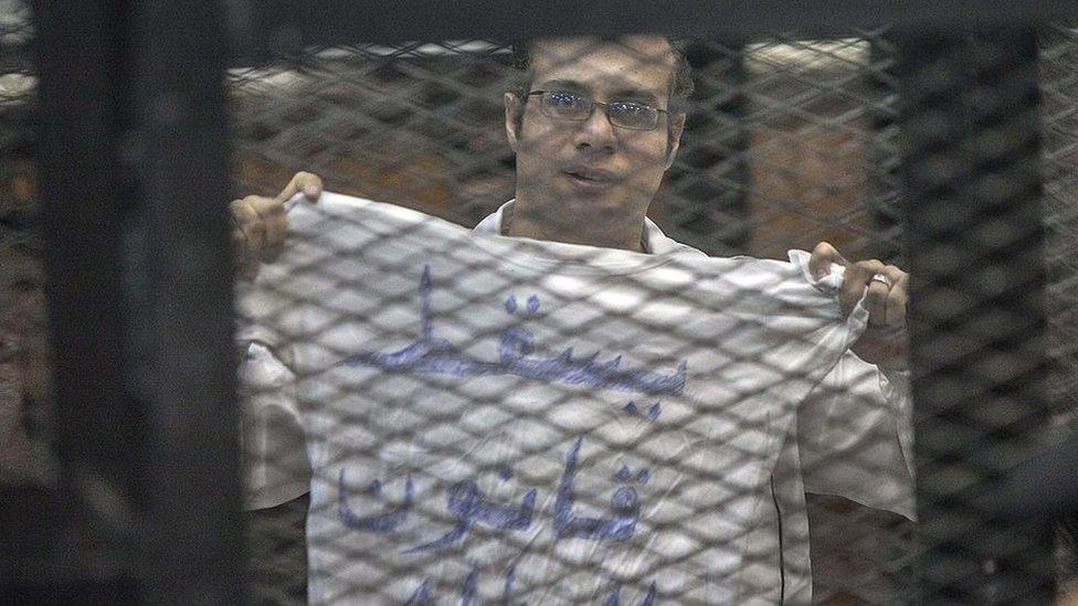 Egyptian activist Ahmed Maher holds up a T-shirt saying "Drop the law on demonstrations" at his trial on 8 December 2013