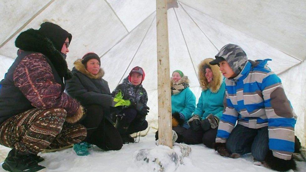 A class of several students gather in a tent, with snow for the ground