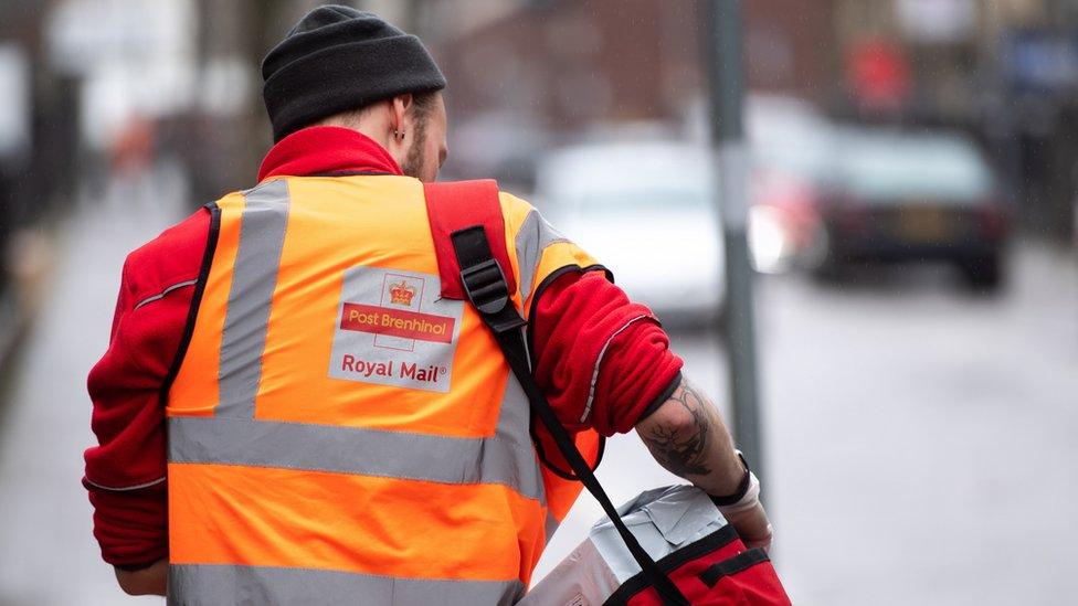 Royal Mail postal worker in uniform walking away from the camera