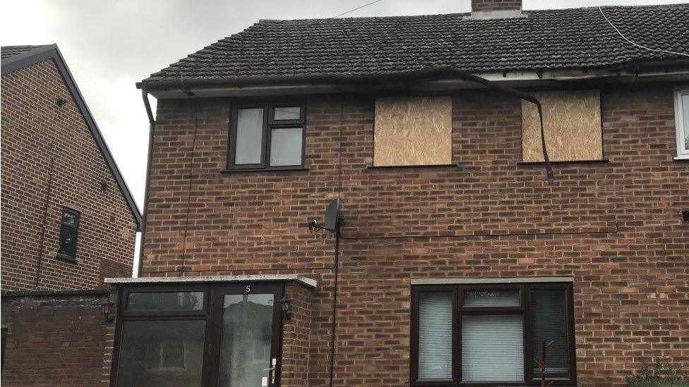 A house with boarded up windown on the upper floor.