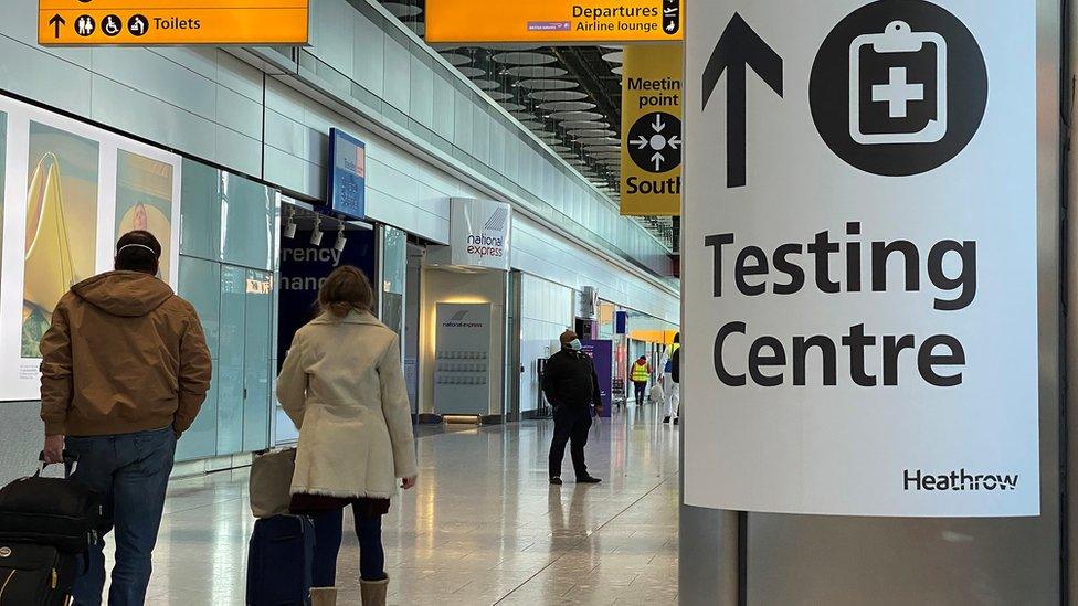 Travellers walking past a testing centre sign at Heathrow Airport