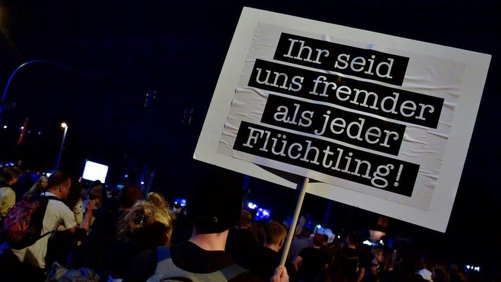 Man holds German sign which reads: "You are more foreign to us than any refugee"