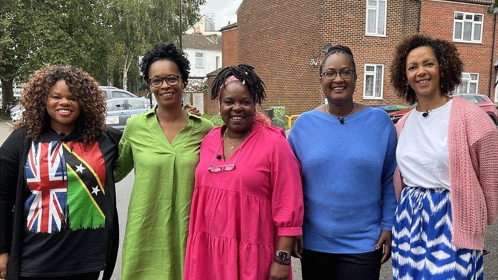 five women stand in a line and hug each other