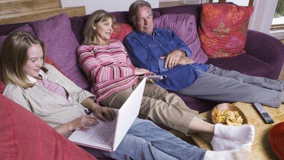 Grandparents watch television while granddaughter uses her laptop