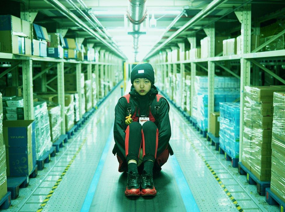 A photo by Cao Fei showing a woman sitting on the floor in a warehouse