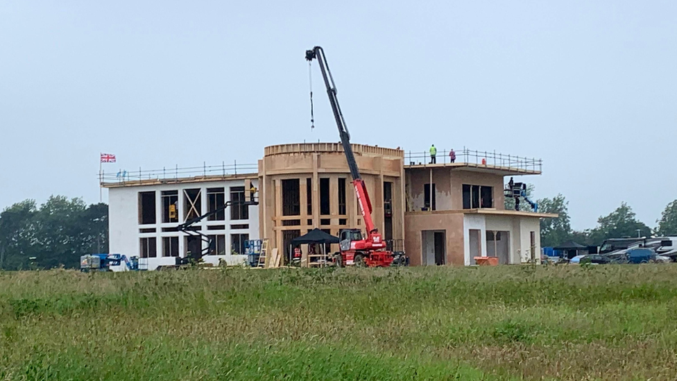 Construction of a two-storey pre-fab buildingon grassland in Bawdsey. A crane can be seen and men in hard hats