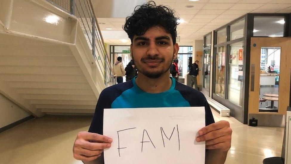 A college student holding up a sign with the slang word "fam"