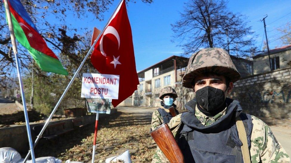 Azeri service members stand guard near state flags of Azerbaijan and Turkey at a checkpoint in Hadrut town on 26 November