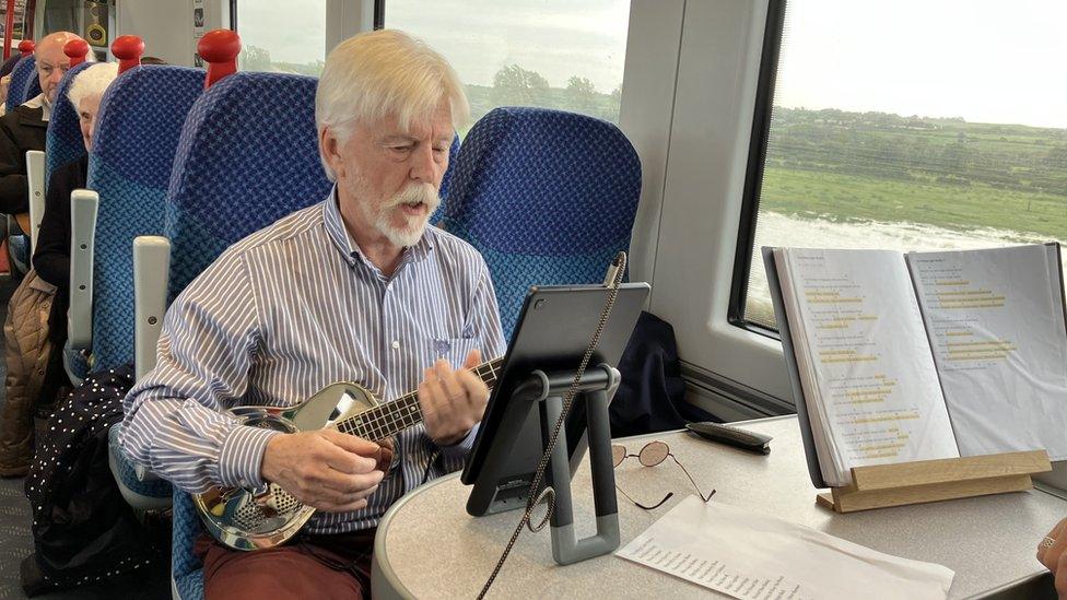 A man plays a ukulele while sitting on a train