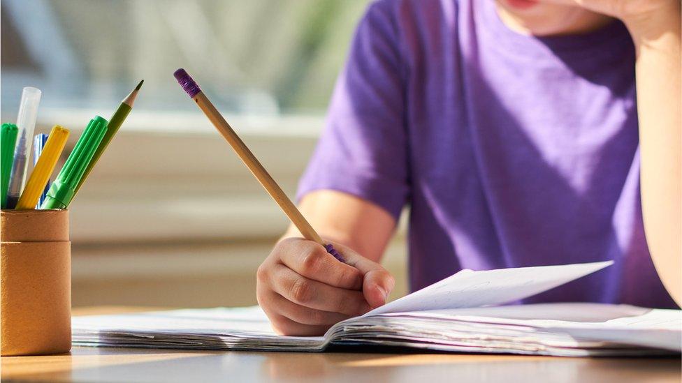 a child is sitting at a desk writing with a pencil