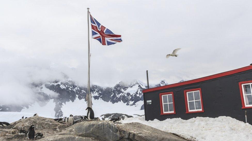 Port Lockroy - icy mountains and penguins on a rock next to a black and red building