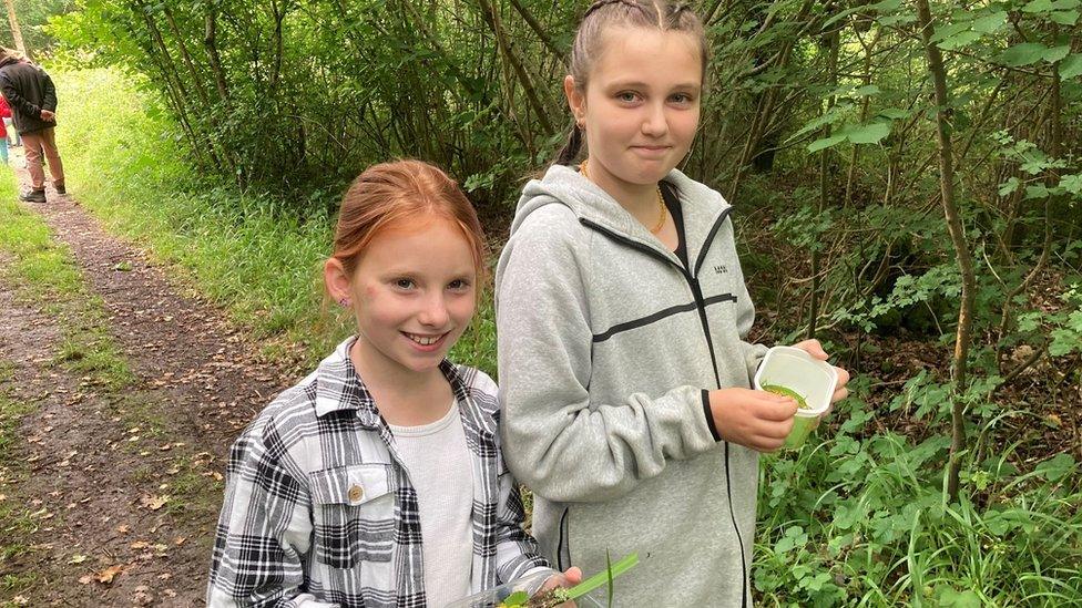 Penny (9) and Ada (10) young carers from Wiltshire standing in Jubilee Woods near Trowbridge holding tubs of items foraged from the woods