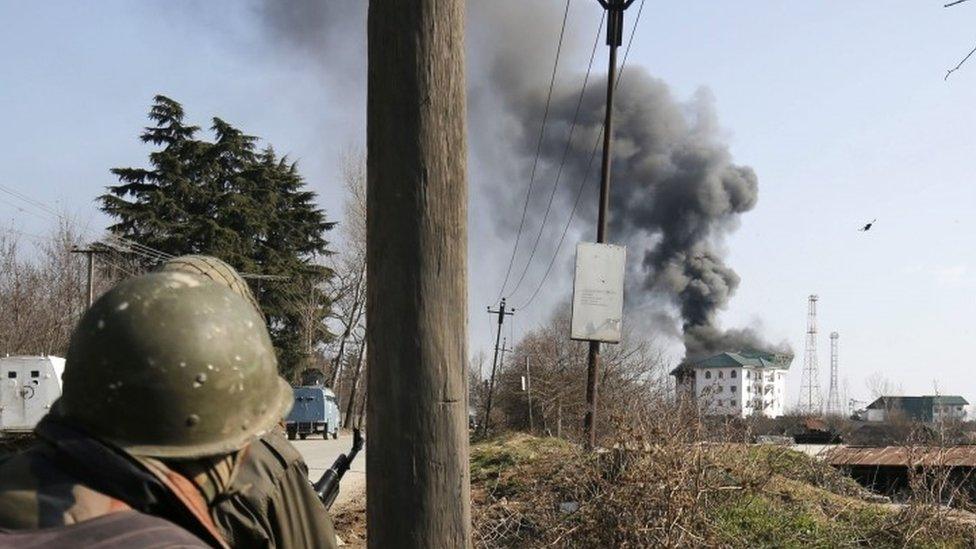 An Indian soldier looks on as columns of smoke come out from the top floor of building where militants are holed up during a gunfight near Srinagar (21 February 2016)