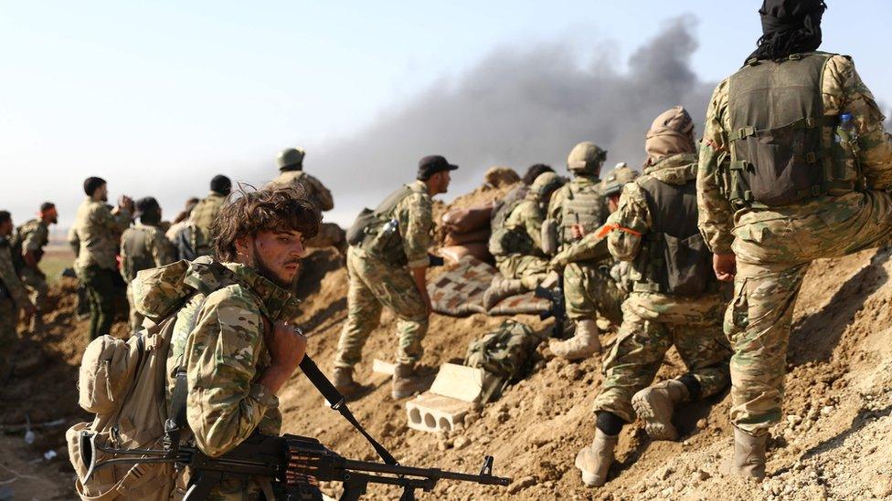 Turkish-backed Syrian rebels and Turkish soldiers watch as smoke rises from the Syrian town of Ras al-Ain on 12 October 2019