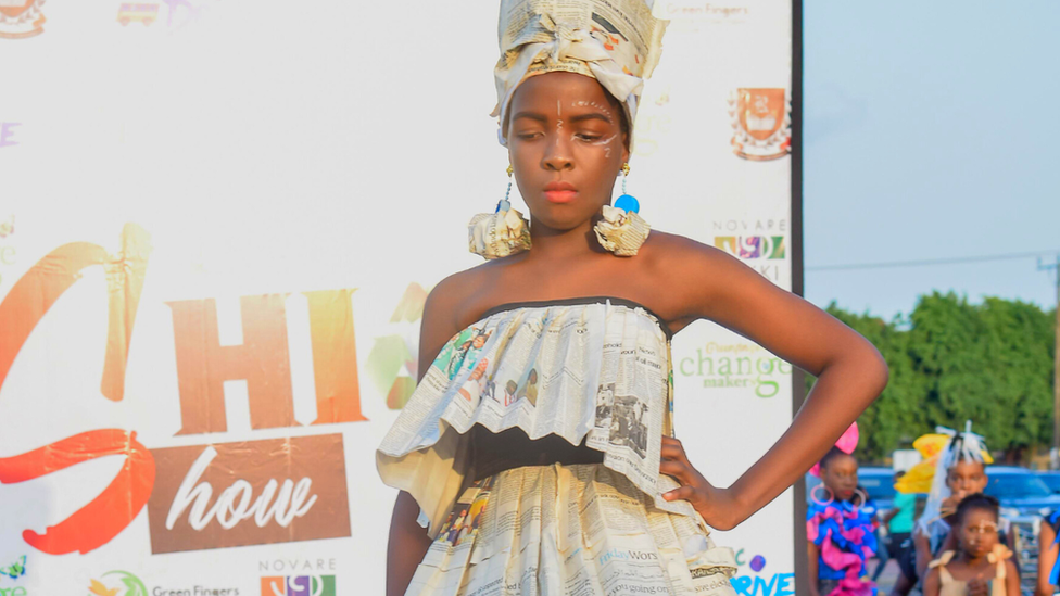 Girl posing on runway in newspaper dress