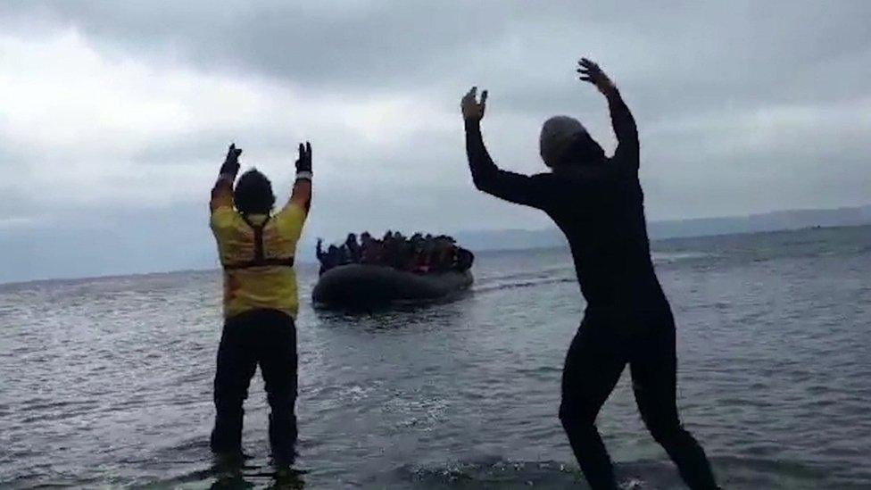 Men waving an inflatable dinghy full of people in to shore