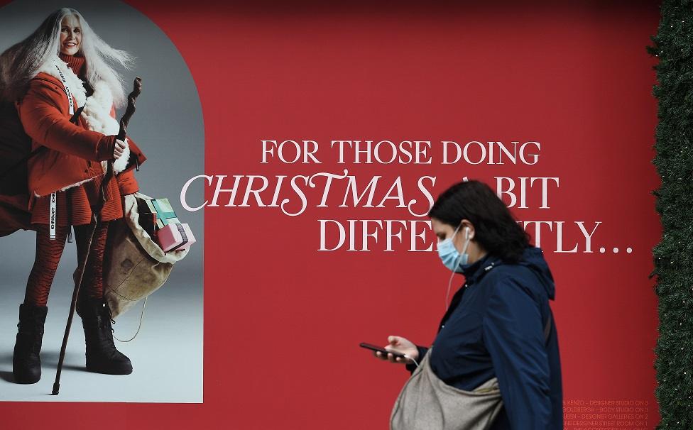 Woman wearing mask walking past Christmas poster