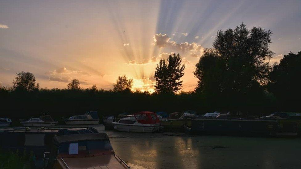 This photo shows boats in the foreground and sun in the background.