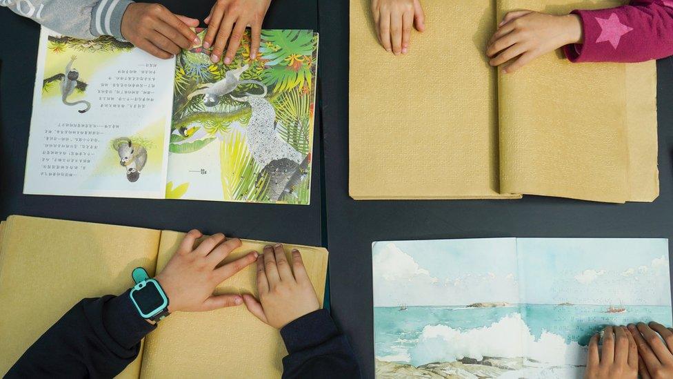 Four open books with children's hands resting on them