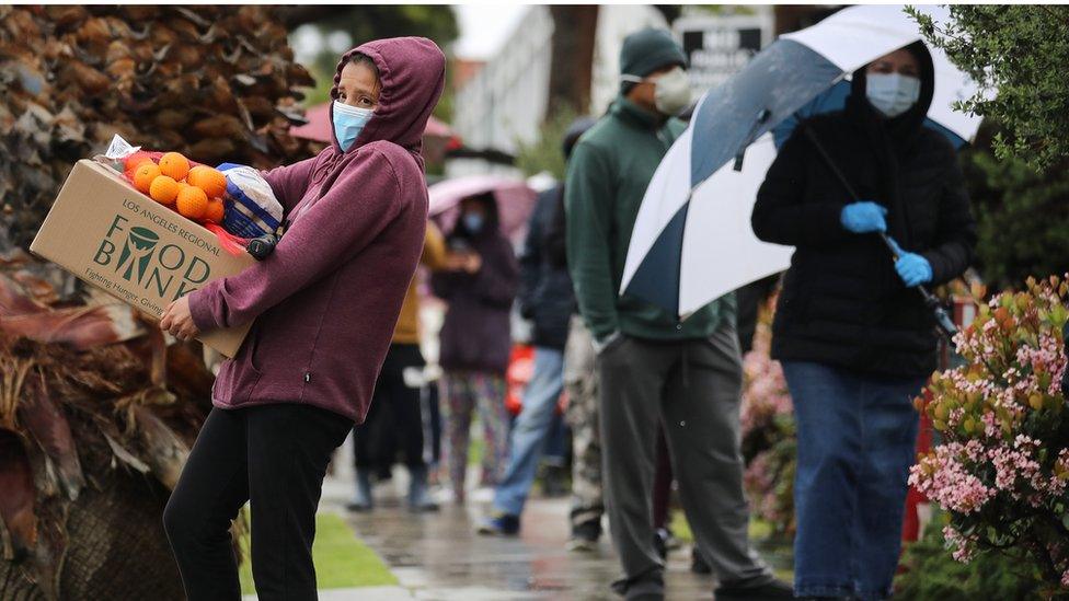 A recipient carries a box of food as others wait in line at a Food Bank distribution for those in need as the coronavirus pandemic continues on April 9, 2020 in Van Nuys, California. Organizers said they had distributed food for 1,500 families amid the spread of COVID-19.