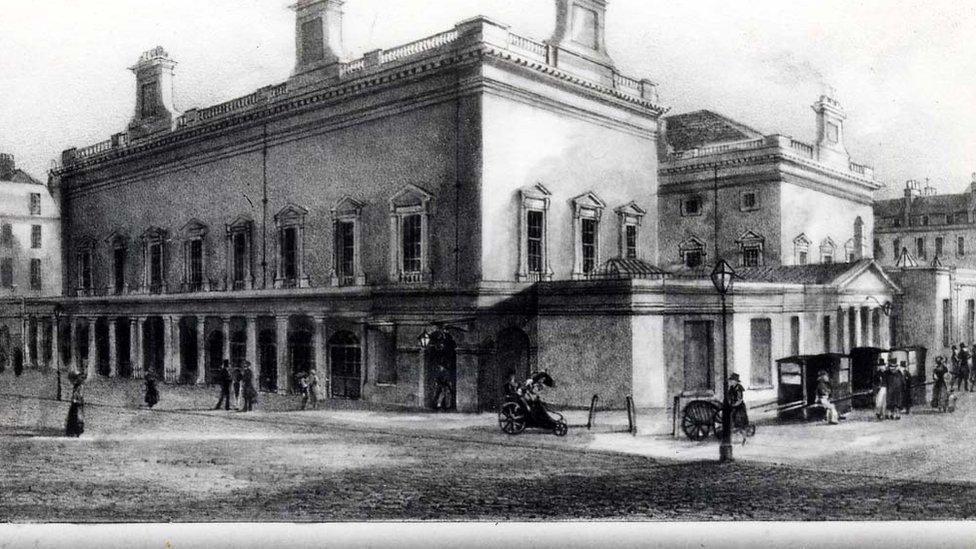 An old engraving of Bath Assembly Rooms, showing people walking outside with sedan chairs.