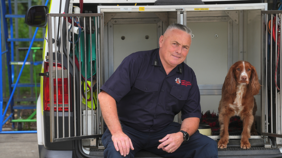 Graham Currie, trainer and handler, sitting next to Fizz the fire dog. Fizz is a spaniel type dog.