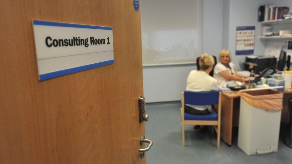 A doctor's consultation room with a GP and a patient sitting inside.