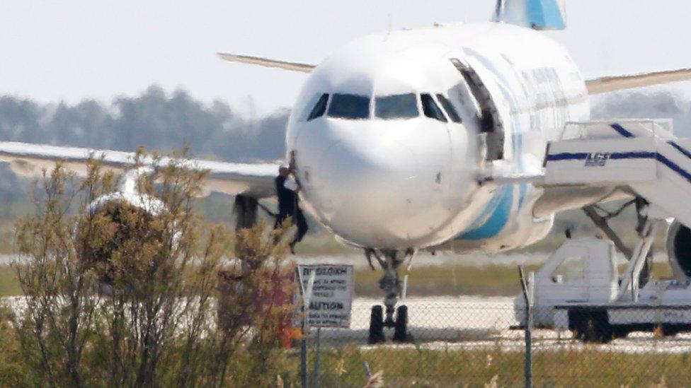 A man climbs out of the cockpit window an EgyptAir Airbus A-320 parked at the tarmac of Larnaca airport after being hijacked and diverted to Cyprus on 29 March 2016