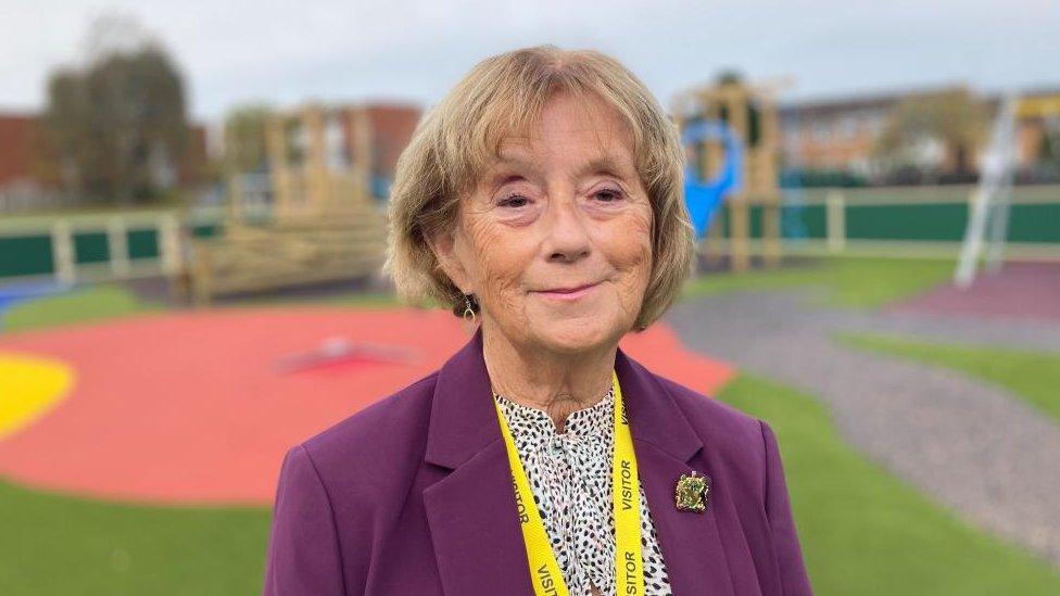 Woman wearing purple jacket stands in a school playground