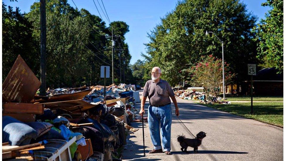 Charles Tripp, of Rome, Georgia, walks Louie down his sister-in-law's street. He came down with family with an RV, supplies, and support. "I am supervision, they're labor," he remarks pointing to family members, "I just had heart surgery." Denham Springs, LA.