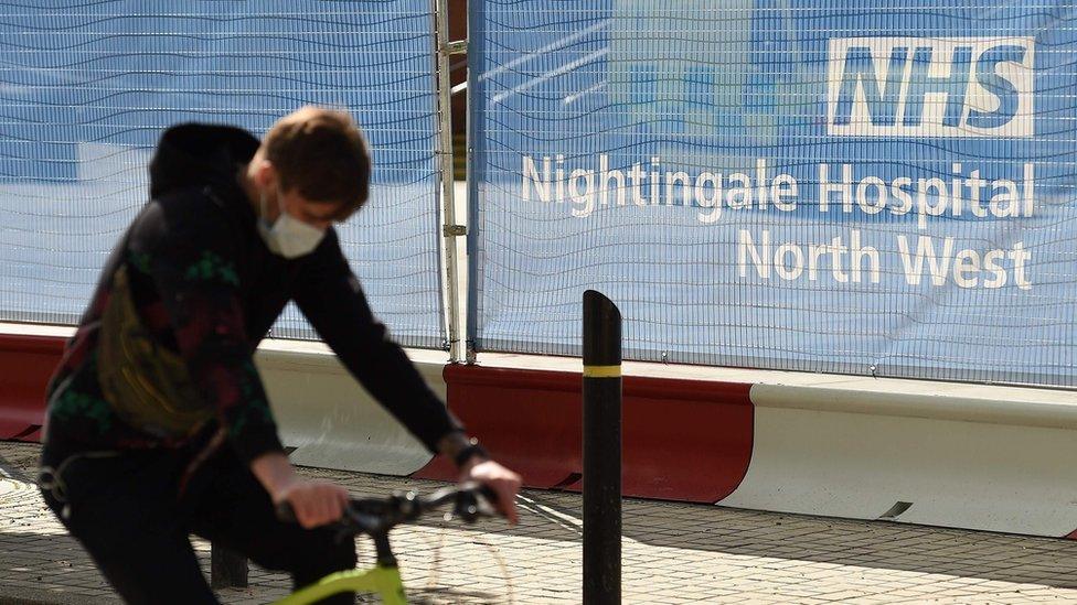 A man wearing a face masks cycles past the NHS Nightingale Hospital North West in Manchester City Centre