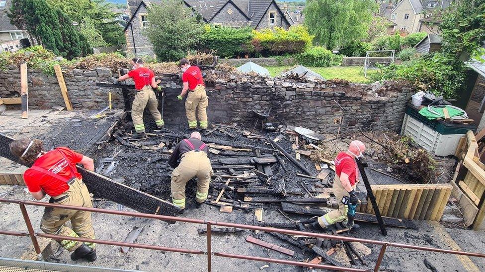 Men in red t-shirts and brown trousers working to replace the burnt shed