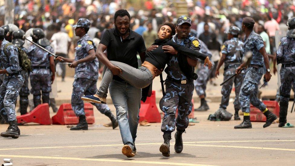 federal policeman and a man carry a woman injured during a protest following the burial ceremony of Simegnew Bekele