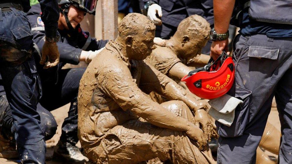 Volunteer rescuers who were attacked by wasps while removing debris to recover the body of a person are attended by firefighters, as the search of missing persons who were swept away on Saturday by devastating floods following heavy rain continues, in Las Tejerias, Aragua state