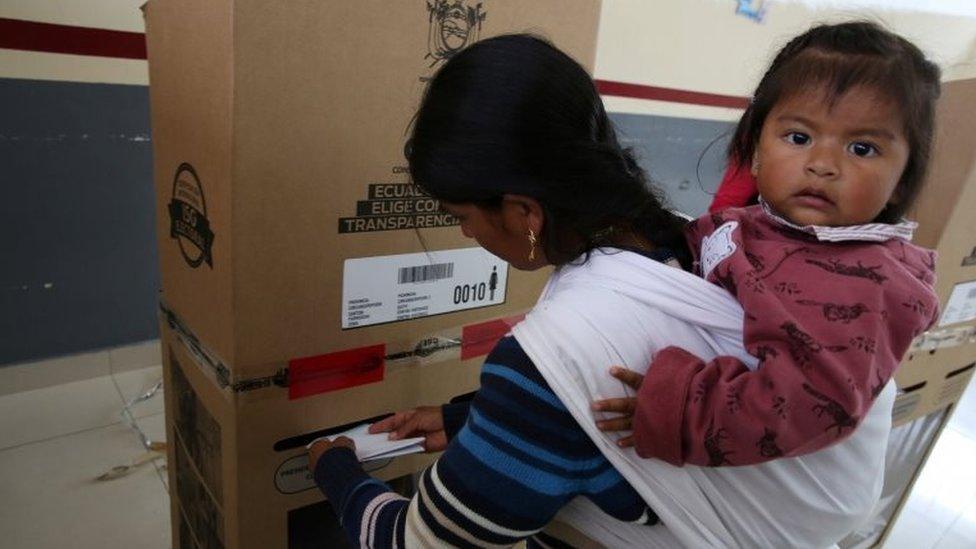 A girl looks on as her mother casts her vote during the presidential election at a school-turned-polling station in Quito, Ecuador February 19, 2017