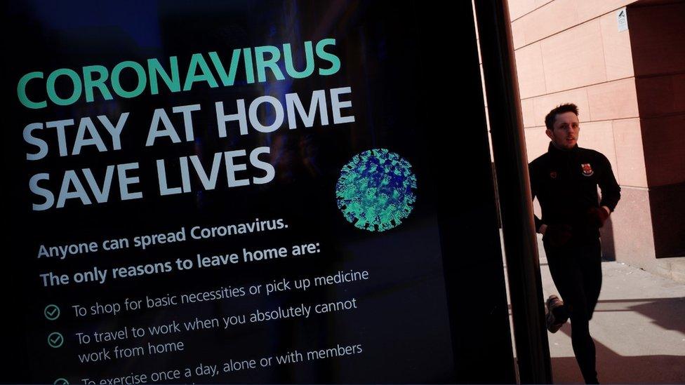 Man running past a coronavirus warning billboard