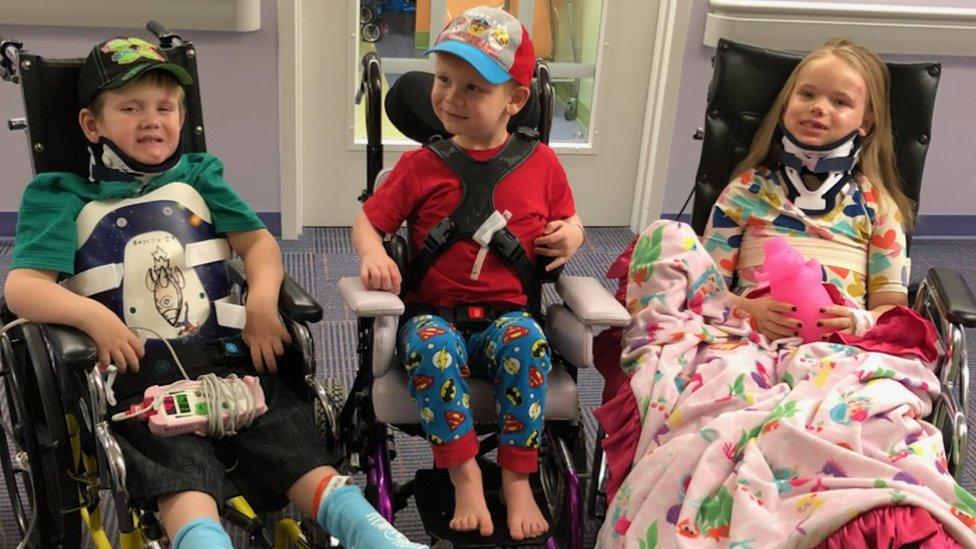 Three children sit together. All are in wheelchairs, with various casts and braces.