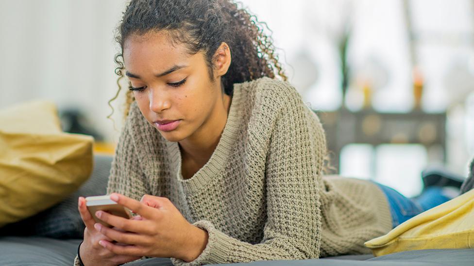 A teenager looks at her phone at home