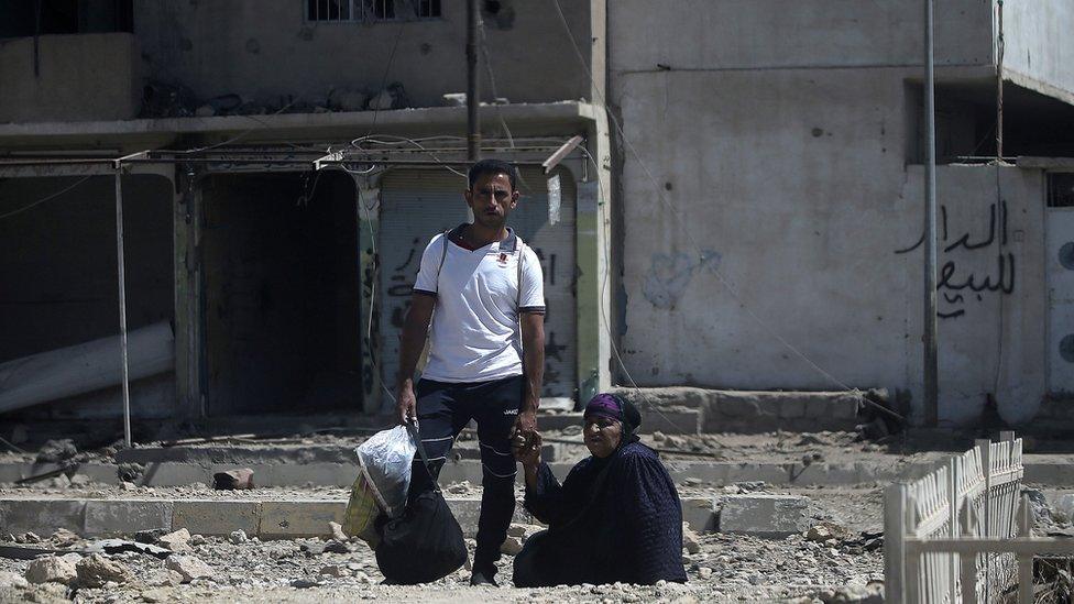 A man holds the hand of an elderly woman as they flee from clashes in western Mosul, 27 May.