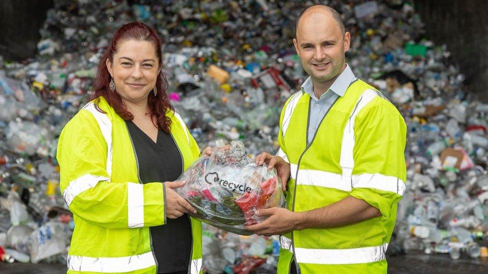 A man and woman wearing high visibility jackets holding plastic waste