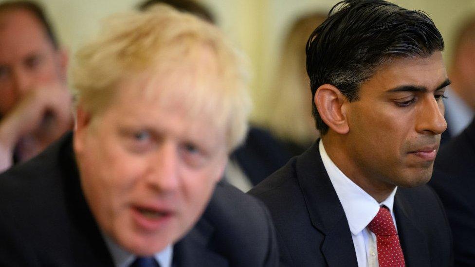 rishi sunak looking concerned sitting next to boris johnson