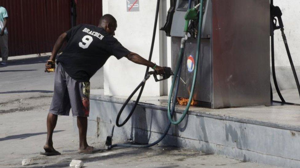 A protester tries to pump gasoline to feed a little fire at a gas station during a demonstration against the electoral process in Port-au-Prince, Haiti, January 18, 2016