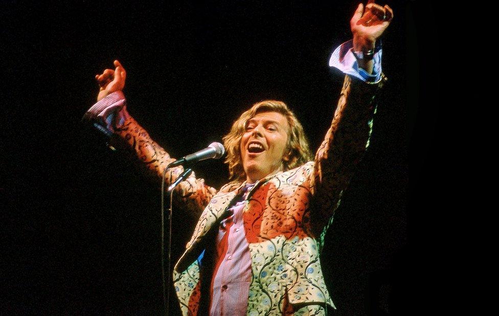 David Bowie holds his hands into the air