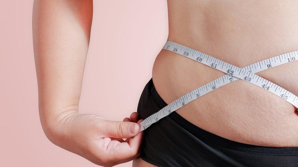 Close up of female measuring her waist with a tape measure.