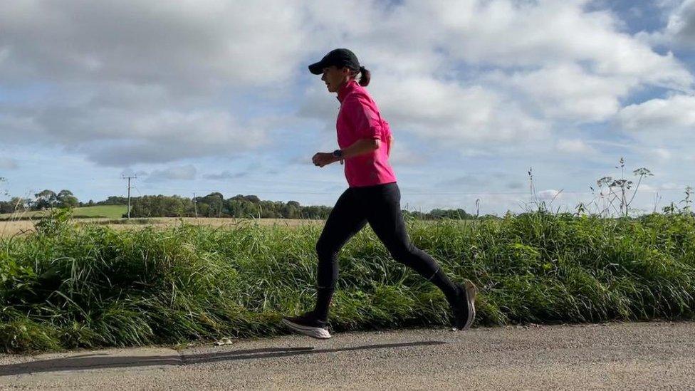 Woman in cap and pink top runs past field